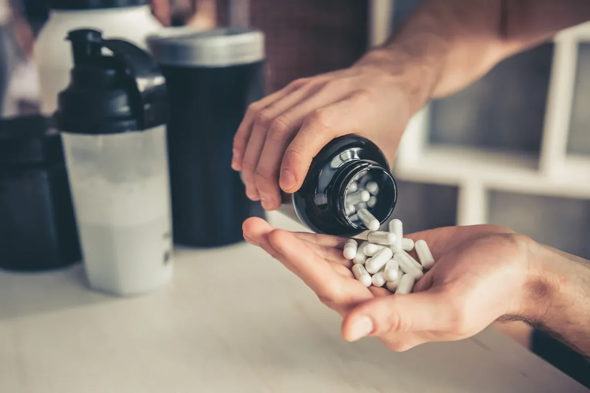 Muskelaufbau Supplement in Kapseln – Mann hält Dose mit weißen Kapseln in der Hand