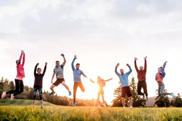 Menschen springen voller Energie auf einer Wiese bei Sonnenuntergang – Symbol für natürliche Vitalität und Lebensfreude