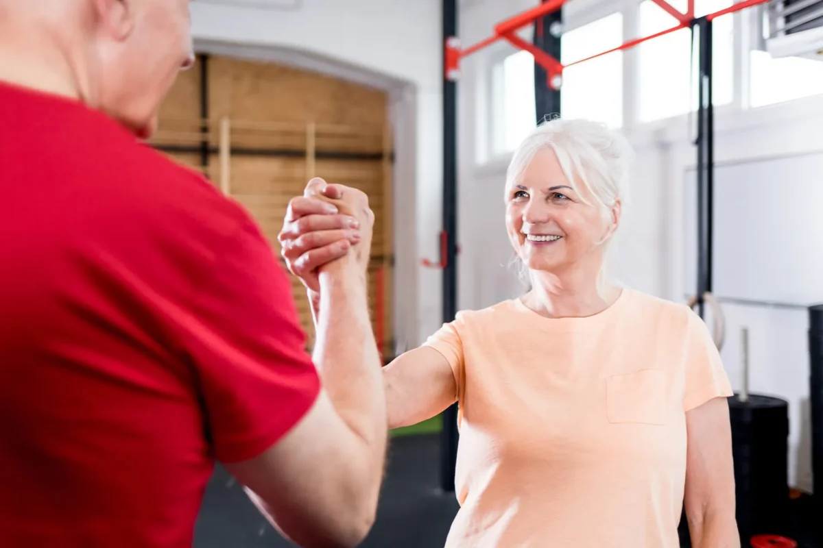 Ältere Frau und Mann geben sich im Trainingsraum die Hand – Symbol für Beweglichkeit und starke Gelenke