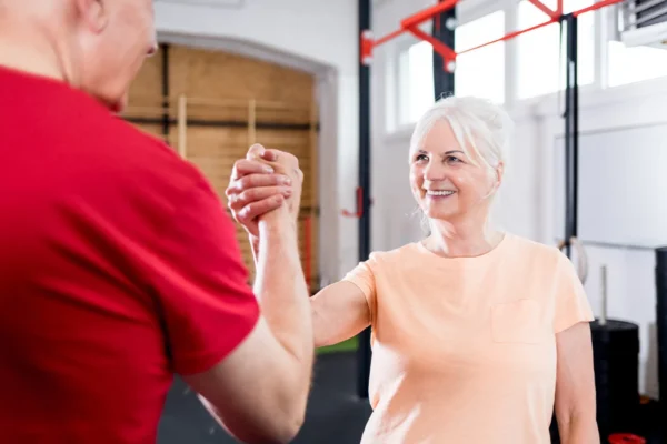 Ältere Frau und Mann geben sich im Trainingsraum die Hand – Symbol für Beweglichkeit und starke Gelenke