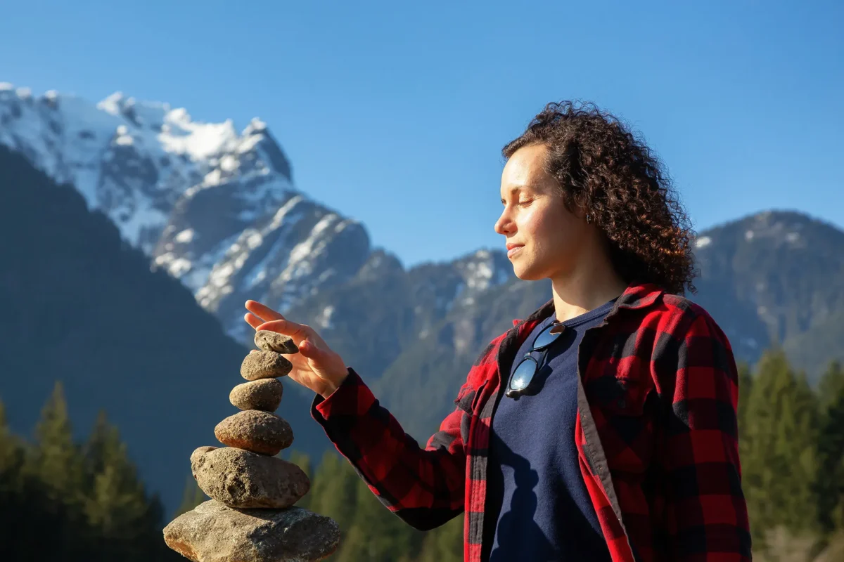 Frau balanciert Steine in der Natur vor Bergkulisse – Symbol für innere Balance und hormonelles Gleichgewicht