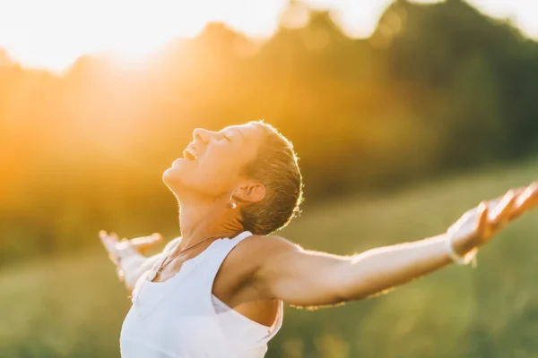 lächelnde Person breitet im Sonnenlicht die Arme aus als Zeichen von Vitalität und Immunsystem unterstützen